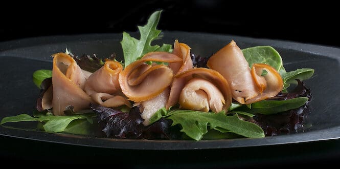 Rolls of smoked albacore tuna lox served on a platter with fresh salad greens.