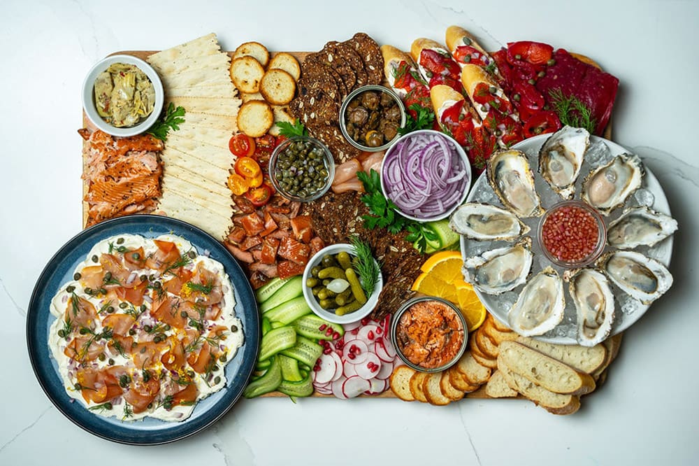 A seafood charcuterie board adorned with fresh oysters, hot smoked salmon, wild smoked scallops, vegetables and more.