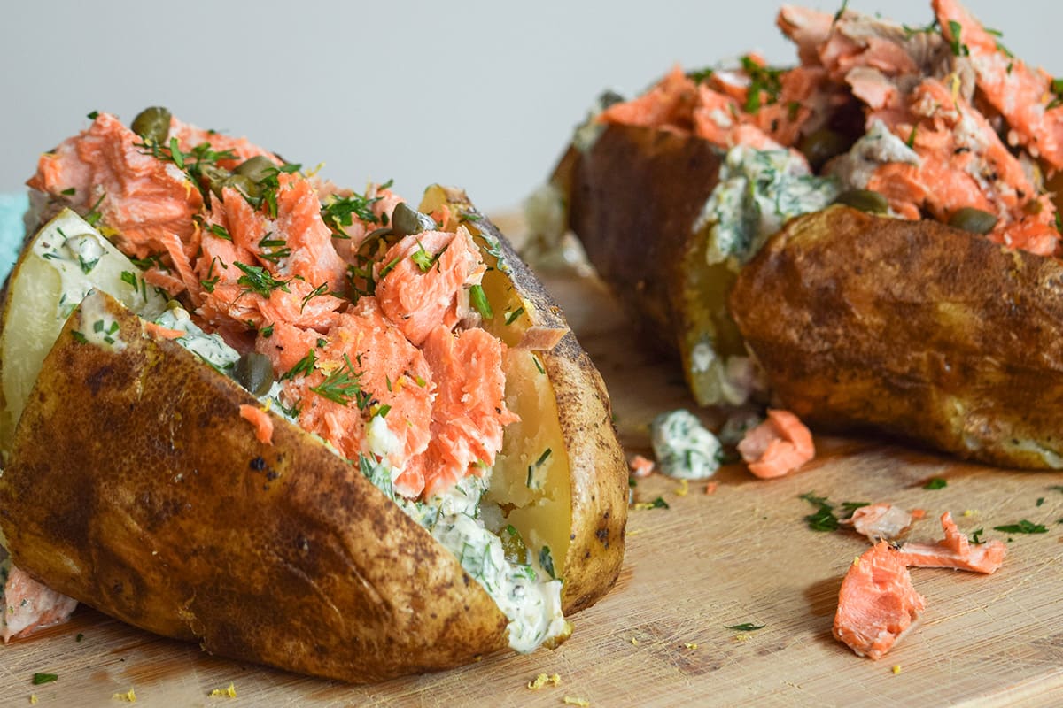 Two baked potatoes topped with flakes of sockeye salmon, dill sauce and capers.