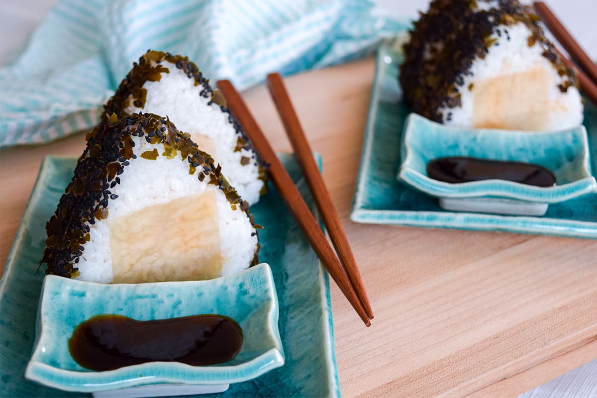Four sockeye salmon-filled onigiri arranged on blue plates with a side of soy sauce.