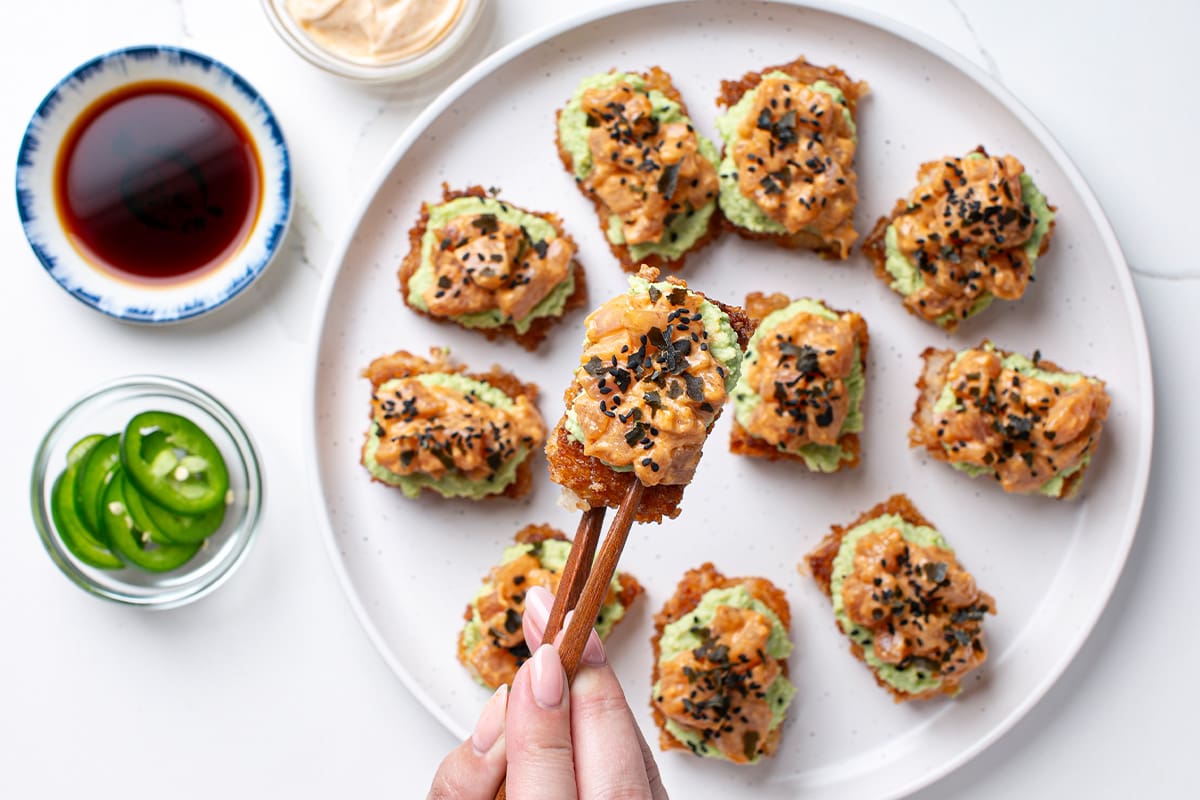 Spicy Albacore tuna crispy rice served on a white plate as an appetizer with sides of soy sauce, jalapeños, and sriracha mayo.