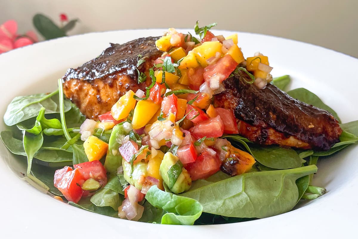 A honey mustard-glazed lingcod fillet served on a bed of spinach with fresh peach salsa.
