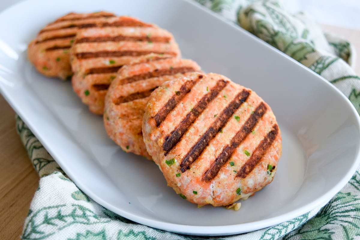 Four grilled salmon patties served on a white plate.