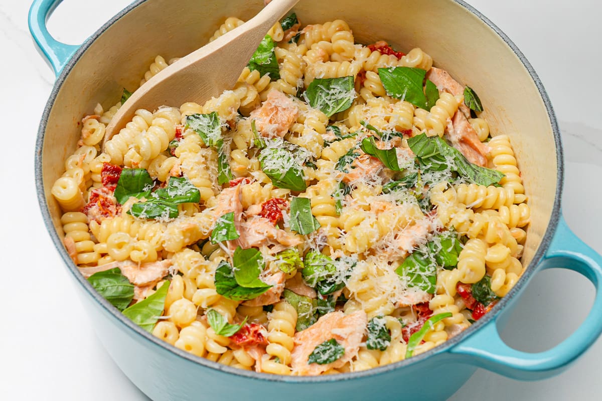 A pot of creamy Tuscan salmon pasta, topped with basil and grated parmesan.