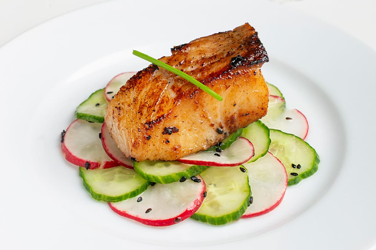 A piece of miso-marinated sablefish plated atop an Asian-inspired cucumber and radish pickle.