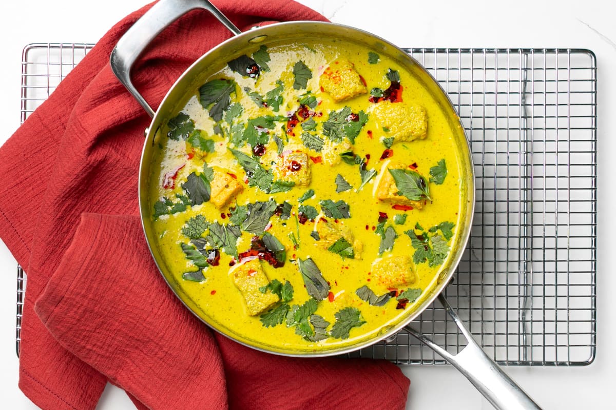 A saucepan of coconut salmon curry, topped with chilli oil, Thai basil and cilantro.