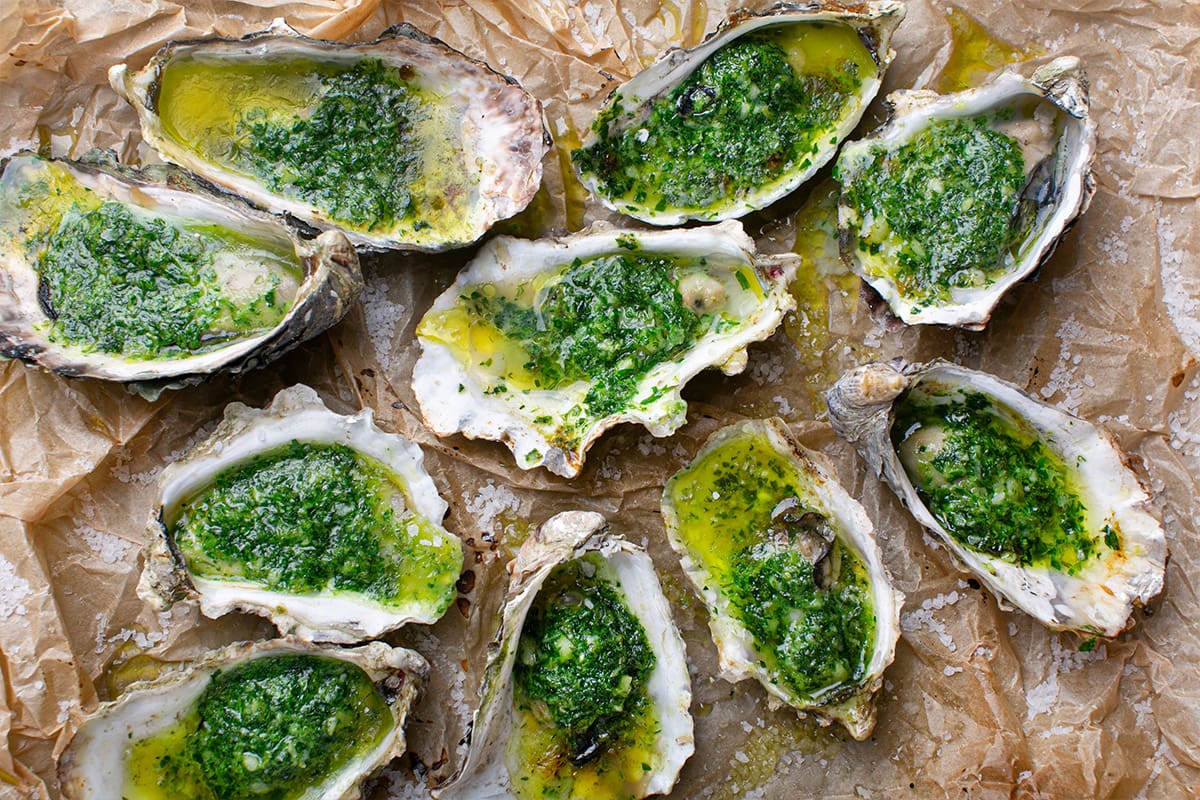 10 Pacific oysters grilled with green herb butter, presented on a tray.