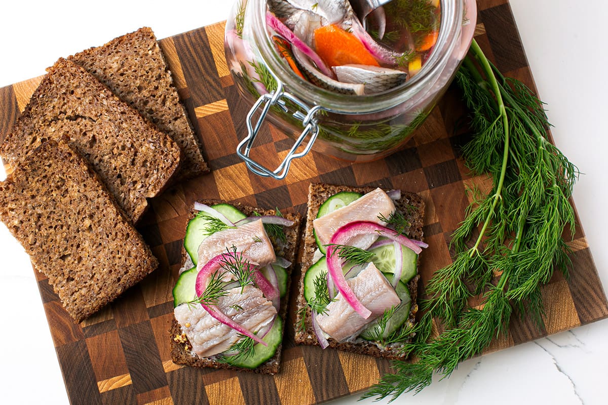 Pickled herring served on top two pieces of dark rye bread with fresh cucumber and pickled red onion.