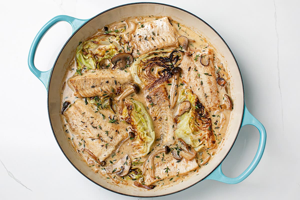 A cast-iron skillet filled with walleye fillets and charred cabbage in a miso mushroom sauce.
